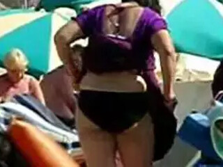 Aunt in swimsuit undresses down on a foreign beach